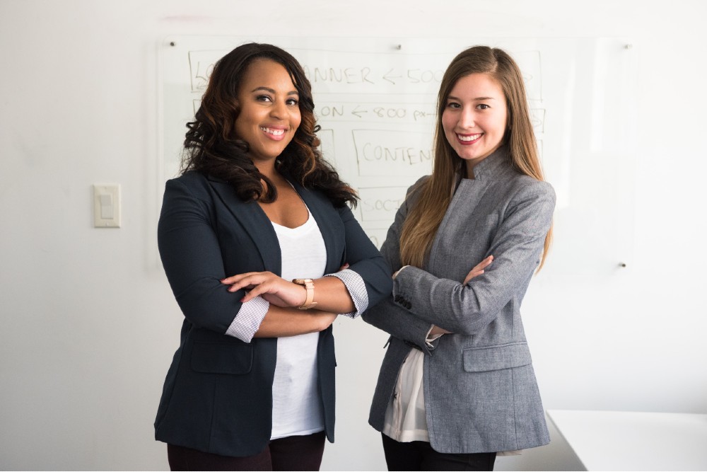 Third Culture Africa Leadership vs Boss two ladies wearing black and beige jacketstanding in a room with white background and some writing in the white board