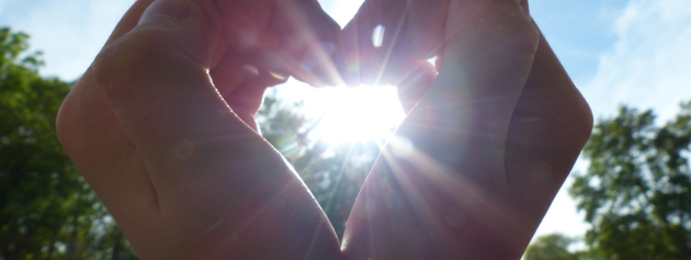 acts of kindness: making a heart with hand in front of the sun